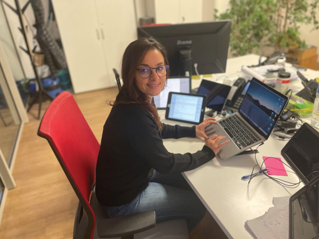 femme souriant travaillant sur un ordinateur avec 3 tablettes et regardant la caméra