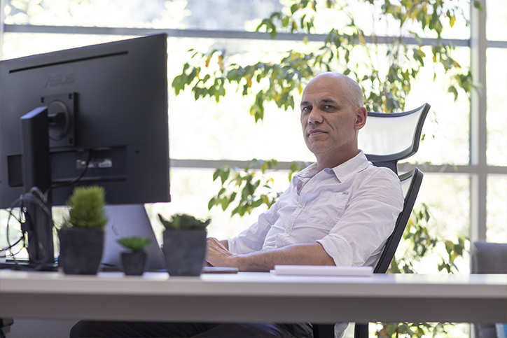 Homme assis à son bureau devant deux ordinateurs et souriant