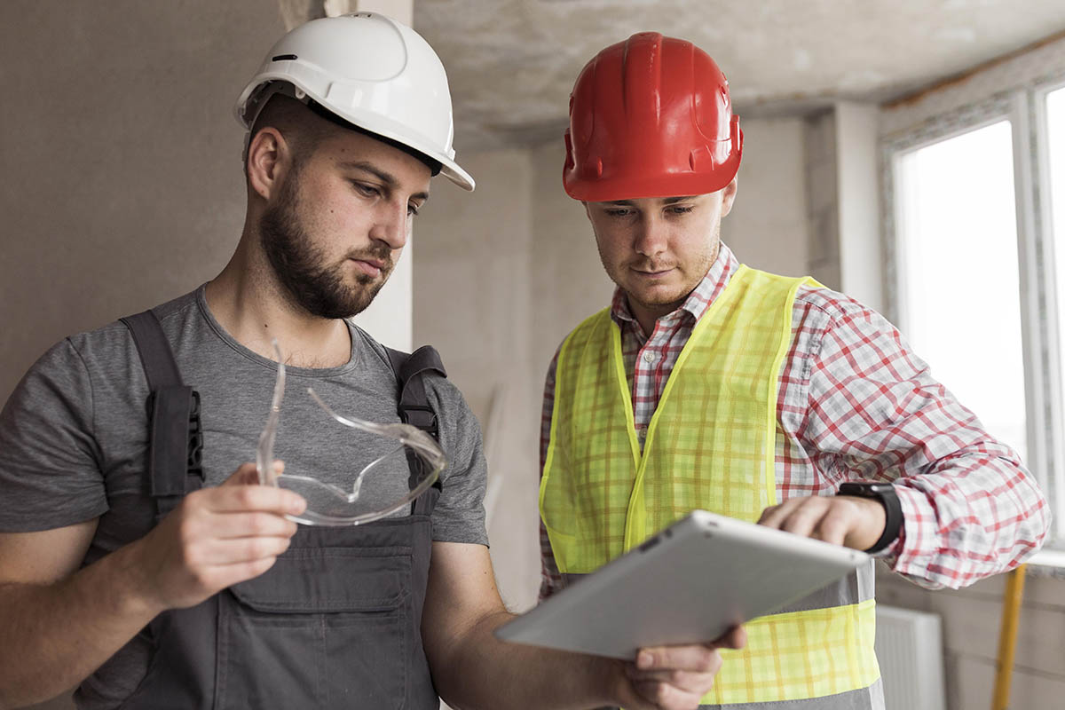 Deux personnes sur un chantier avec un iPad à la main portant un casque et une veste de chantier