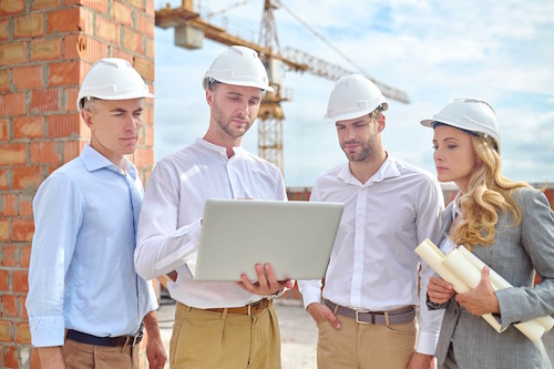 4 personnes entrain de discuter avec un casque de chantier et un ordinateur et des plans dans les mains
